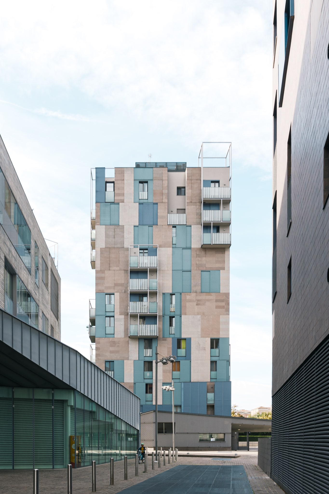 Edificio residenziale incorniciato da volumi bassi, con facciata in pietra e pannelli azzurri