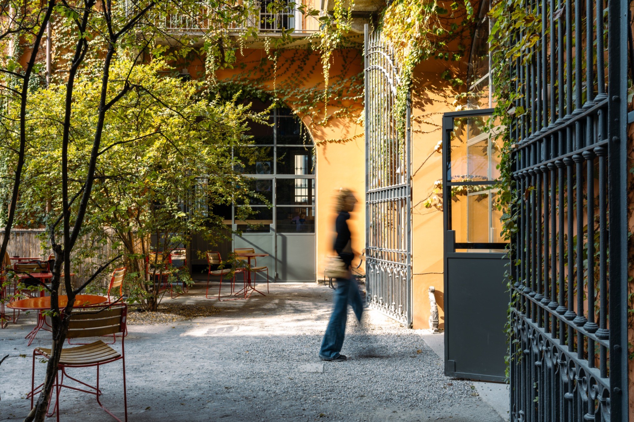 Cortile con vegetazione e pareti color ocra attraversato da una figura in movimento
