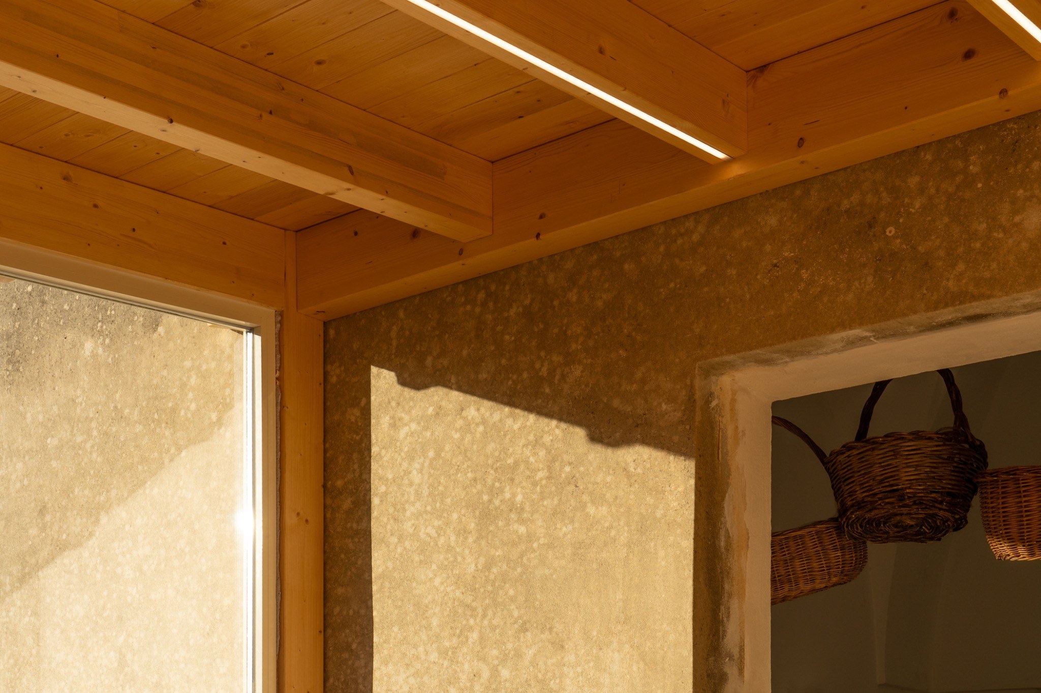 Interno con soffitto in legno, pareti materiche e un rettangolo di luce naturale