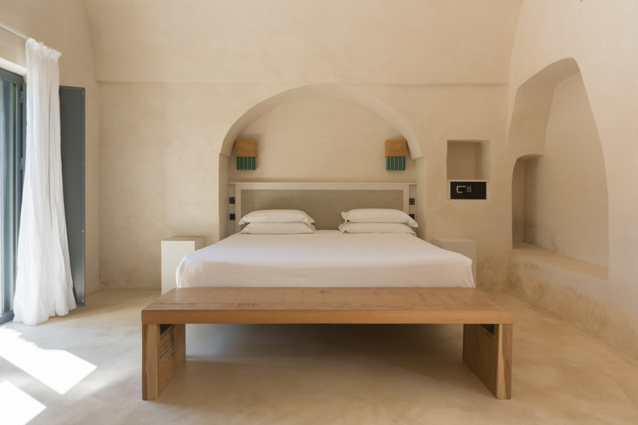 Camera dai toni chiari con letto, panca in legno, nicchie e grandi archi intonacati