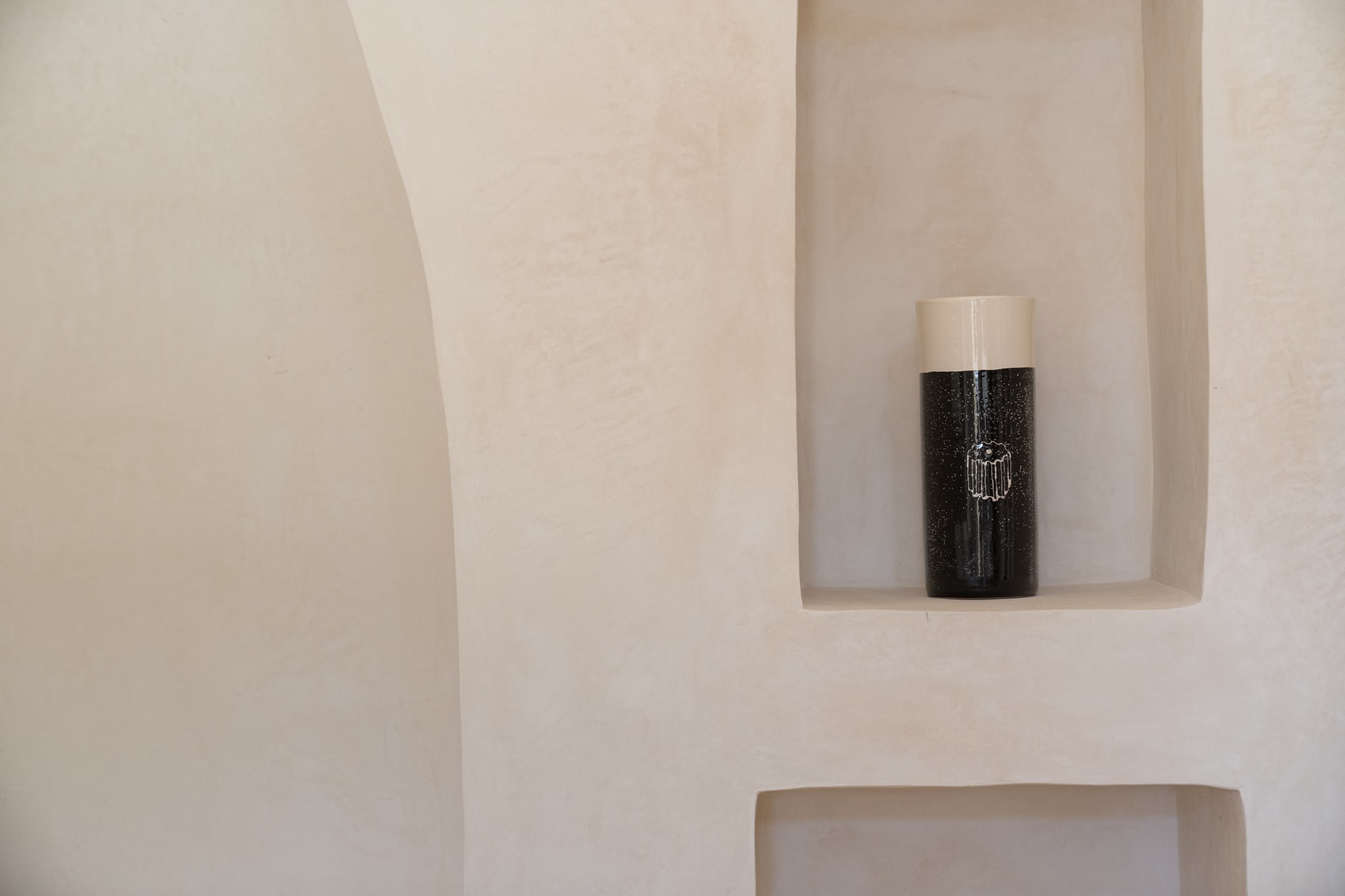Vaso nero e bianco in una nicchia tra pareti intonacate e profili curvi